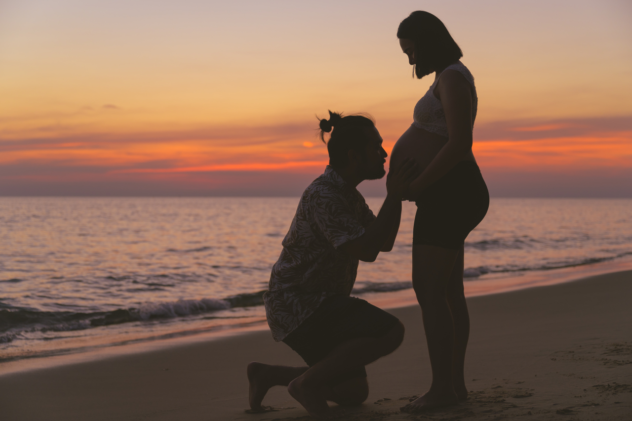 Young family and pregnant wife spend holiday on the beach at sunset